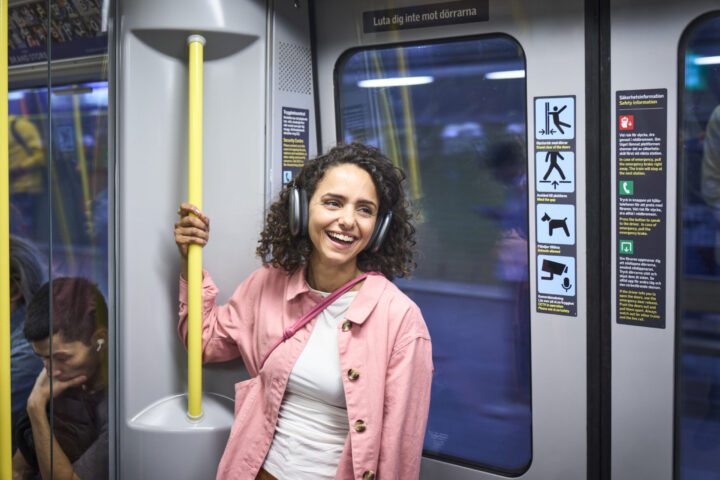 Glad kvinna åker tunnelbana och lyssnar på musik i hörlurar